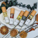 Five small bottles with labels on a white dish, surrounded by dried oranges and lavender.