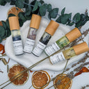 Set of small bottles with bamboo caps on a white tray surrounded by dried oranges and eucalyptus leaves.
