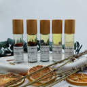 Five small bottles of Wildroot Alchemy essential oils on a white surface with dried oranges and herbs.