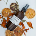 Brown spray bottle labeled 'Fresh Bloom' surrounded by dried orange slices and herbs on a white background