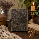 Decorative leather notebook with butterfly design on a wooden surface with candles and books.