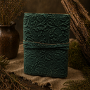 Green embossed leather notebook on a rustic wooden surface with plants.