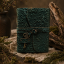 Decorative green leather journal with embossed design on a rustic wooden surface with plants.