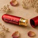 A red cylindrical cosmetic tube labeled 'Wildroot Alchemy Ignite & Rise' with a gold metallic collar, shown next to its matching red cap on a beige textured surface with dried flowers and petals.