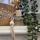 Decorative item with a rope and glass container on a white surface, with green plants in the background.