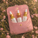 Pink pouch with three small dropper bottles is sitting in a field of flowers