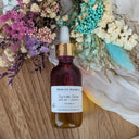 Bottle of serum with a gold cap on a wooden surface surrounded by dried flowers
