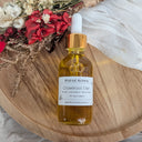 Bottle of Wildroot Alchemy Crownroot Elixir on a wooden surface with flowers in the background