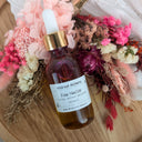 Bottle of Fae Nectar with a dropper on a wooden surface surrounded by flowers