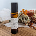 Small amber-colored bottle with a black cap on a wooden surface, surrounded by dried flowers and herbs.