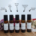 Set of small bottles labeled for various wellness purposes on a wooden surface with flowers in the background.