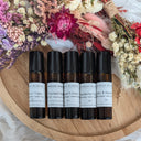 Set of roller bottles with labels on a wooden tray surrounded by flowers