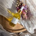 Bottle of yellow liquid with dropper on a wooden surface with dried flowers.