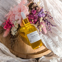 Yellow dropper bottle with a label on a wooden stand surrounded by flowers
