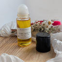 Bottle of Golden Facial Oil with a white cap on a wooden surface, surrounded by flowers and fabric.