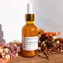 Orange bottle with dropper labeled 'Lover's Aura' on a wooden surface with dried flowers.