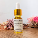 Bottle of Wildroot Alchemy Velaria Bloom on a wooden surface with flowers in the background