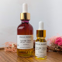 Two bottles of Wildroot Alchemy Sylvan Glow body oil on a wooden surface with dried flowers.