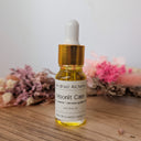 Bottle of 'Moonlit Calm' oil with a dropper on a wooden surface with flowers in the background