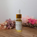 Bottle of 'Beat The Chik' oil with a dropper on a wooden surface with flowers in the background