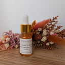 Bottle of Wildroot Alchemy 'Lover's Aura' oil with dried flowers on a wooden surface