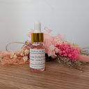 Small bottle with dropper labeled 'Love Potion No. 13' on a wooden surface with flowers in the background