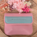 Pink pouch with teal accent on a wooden surface with pink flowers.