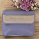 Purple pouch with beige flap featuring 'Wildroot Alchemy' on a wooden surface with dried flowers.