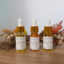 Three bottles of Wildroot Alchemy oils on a wooden surface with dried herbs in the background.