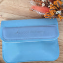 Blue pouch with 'Wildroot Alchemy' branding on a wooden surface with dried flowers.