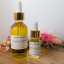 Two bottles of Wildroot Alchemy Botanical Quench on a wooden surface with flowers in the background.