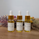 Three dropper bottles with labels on a wooden surface with dried plants in the background