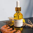 Bottle of Wildroot Alchemy Crown Root Elixir with a dropper on a dark surface with dried plants.