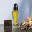 Skincare serum bottle with a black cap and gold base on a wooden surface with dried flowers.