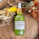 Green bottle with dropper labeled 'Pine Ridge' by Wildroot Alchemy on a wooden surface with dried flowers.