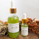 Two bottles of Wildroot Alchemy Pine Ridge product on a wooden surface with dried plants.