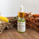 Bottle of Wildroot Alchemy Pine Ridge oil with a dropper on a wooden surface with dried plants.
