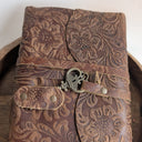 Brown leather journal with floral patterns on a wooden surface