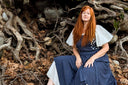 Woman in a blue dress sitting among roots and leaves